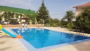 A swimming pool with a slide, surrounded by greenery and a covered seating area. - Villa L'orangeraie, Wilaya de Tlemcen (Tlemcen)