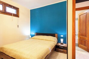 Une chambre à coucher comprenant un lit, une table de chevet, une lampe et une porte donnant sur une salle de bain.