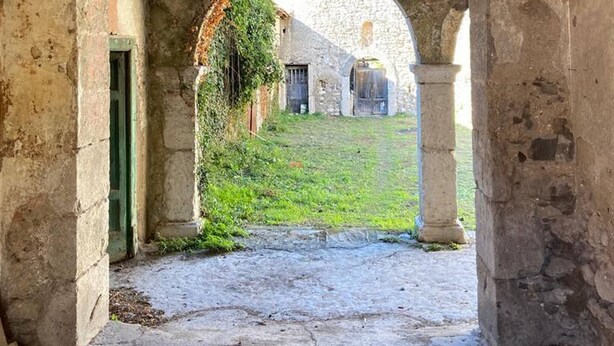 Un corredor de piedra en arco con una zona verde y un edificio al fondo.