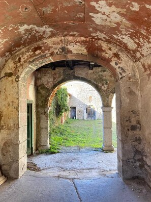 Un corredor de piedra en arco con una zona verde y un edificio al fondo.