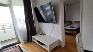 A modern hotel room with a flat-screen TV mounted on a white console table, a wooden bed, and a balcony with a view. - Features of Good And Night (Neuss)