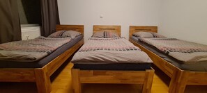 A room with three wooden beds aligned against a white wall, each with a patterned bedspread and pillows. - Features of Good And Night (Neuss)