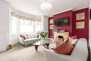 A living room with a sofa, a glass coffee table, a fireplace, and a TV mounted on the wall. - Beautiful Edwardian Home In Central Oxford (Oxford)
