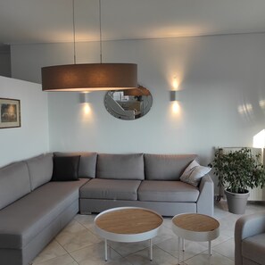 Una sala moderna con un sofá seccional gris, dos mesas redondas de centro con tapas de madera y un espejo grande en la pared.