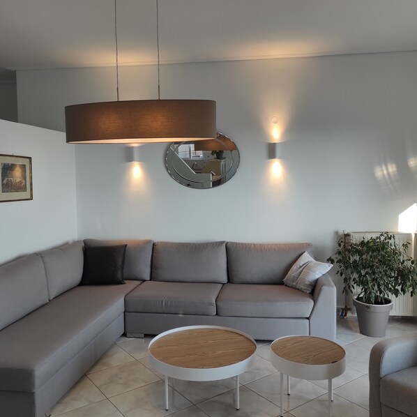 Ein modernes Wohnzimmer mit einem grauen Ecksofa, zwei runden Couchtischen mit Holzbeschlägen und einem großen Spiegel an der Wand.