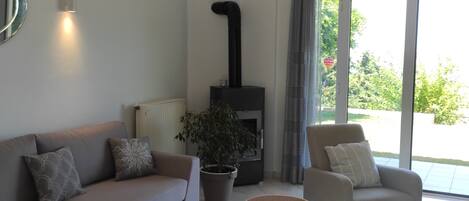 Een moderne woonkamer met een bank, twee fauteuils, een salontafel, een open haard en een groot raam.