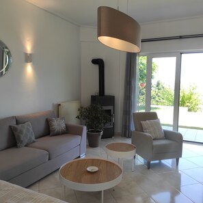 Ein modernes Wohnzimmer mit einer Couch, zwei Sesseln, einem Couchtisch, einem Kamin und einem großen Fenster.