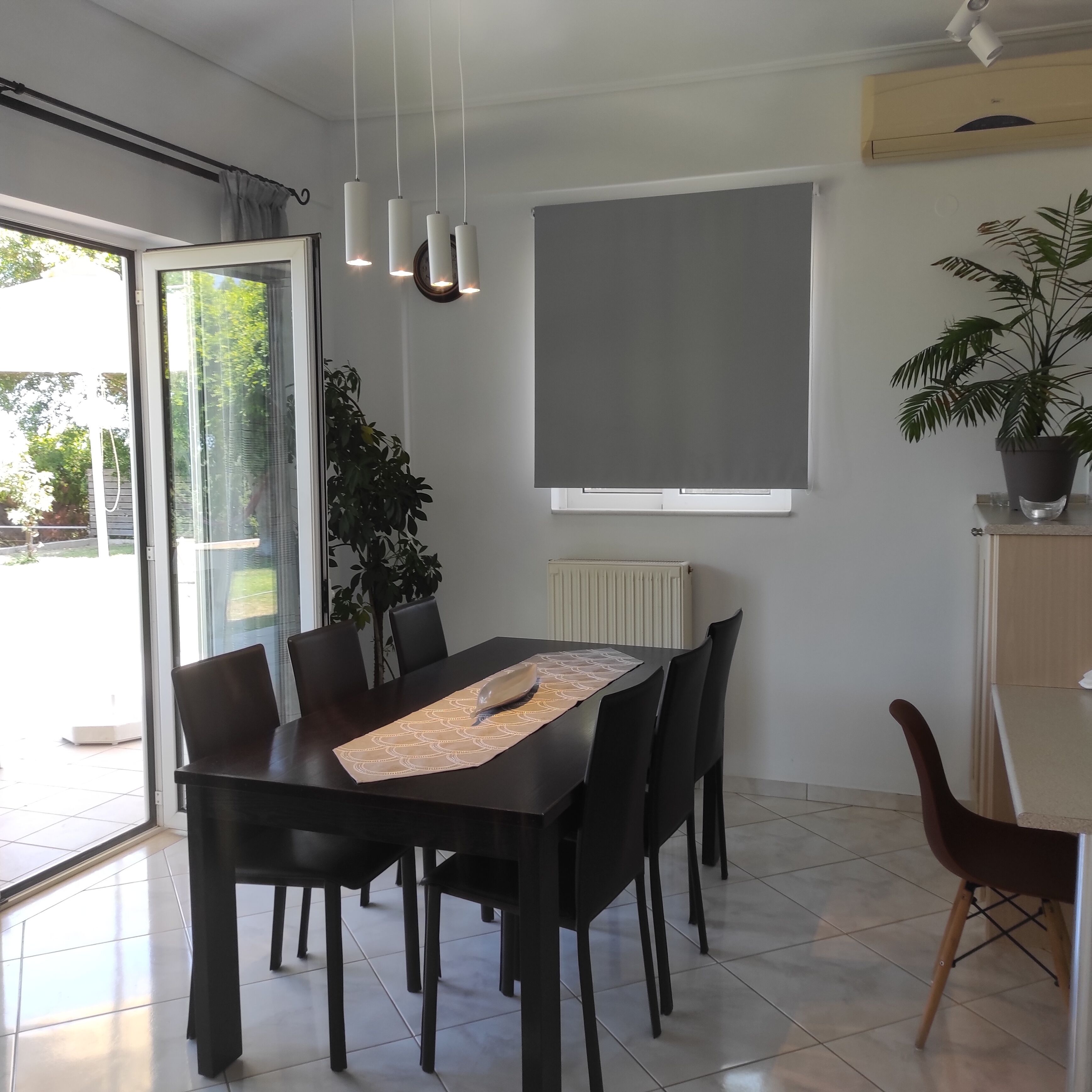 Un coin repas avec une table dressée pour six personnes, une plante en pot et une grande fenêtre donnant sur un paysage verdoyant.