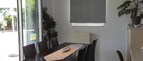 Un coin repas avec une table dressée pour six personnes, une plante en pot et une grande fenêtre donnant sur un paysage verdoyant.
