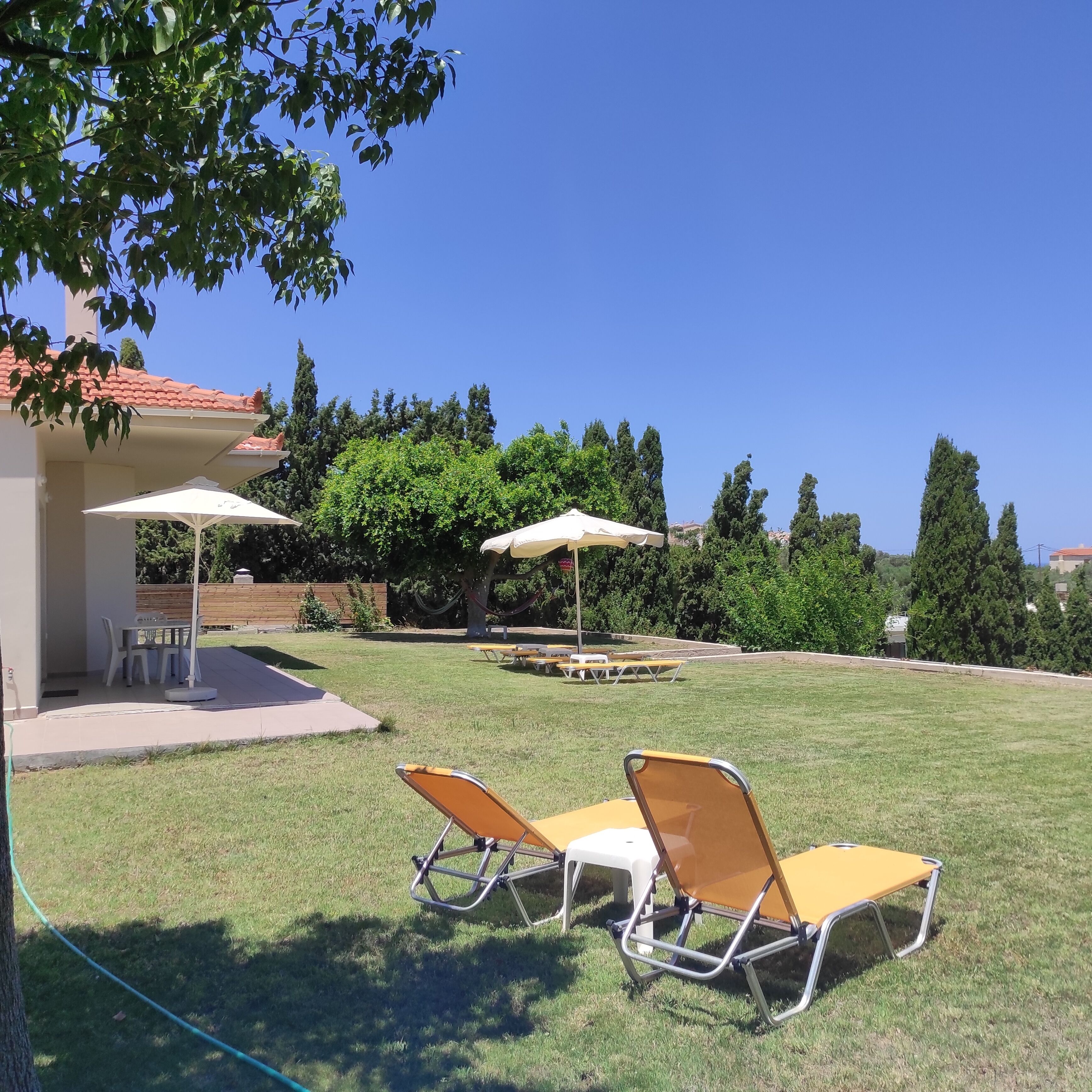 Ein Garten mit zwei Liegestühlen, einem Tisch und einer überdachten Sitzgelegenheit.