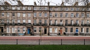 Eine Reihe traditioneller Reihenhäuser mit einheitlicher Architektur, einer roten Backsteinfassade und einem schwarzen Metallzaun im Vordergrund.