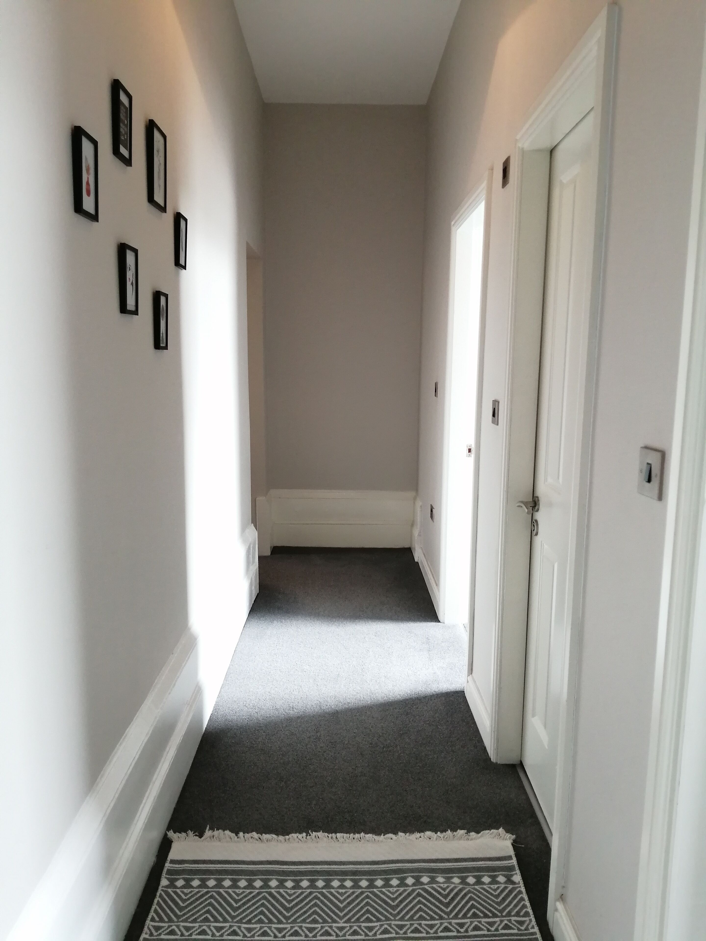 A narrow hallway with a carpeted floor, white walls, and a door on the right.