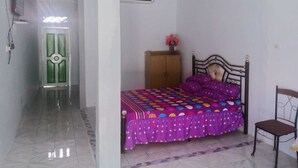 A bedroom with a bed, a wooden wardrobe, a chair, and a door.