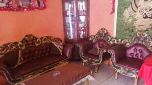 A traditional living room with ornate furniture, including a sofa and two armchairs, a cabinet with glass doors, and a tiled floor.