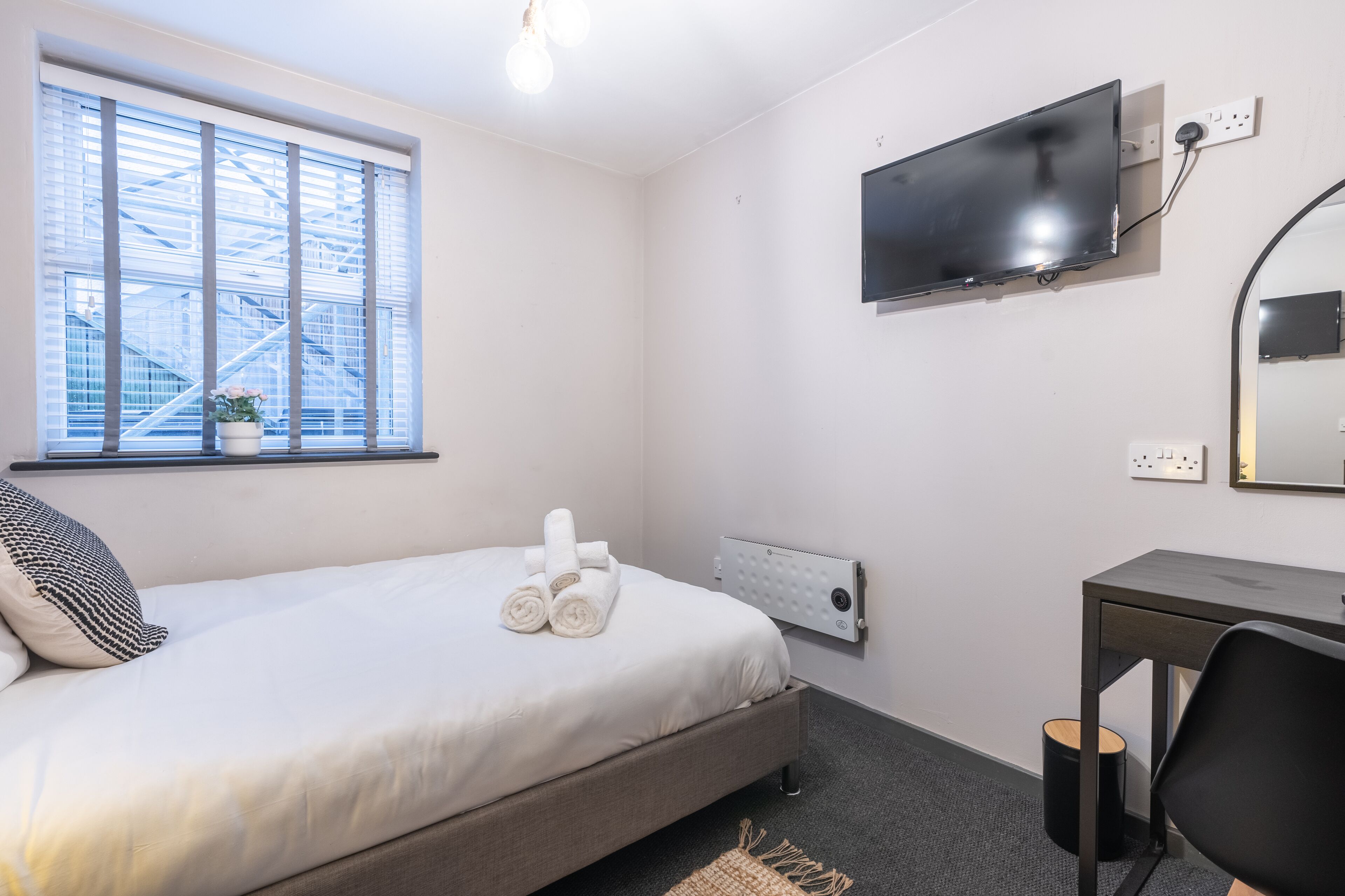 A hotel room with a bed, a desk, a TV, and a window with blinds.