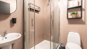 A bathroom with a glass-enclosed shower, a sink, a toilet, and a shelf with a plant. - Woodbury 2-4 (Lancaster)