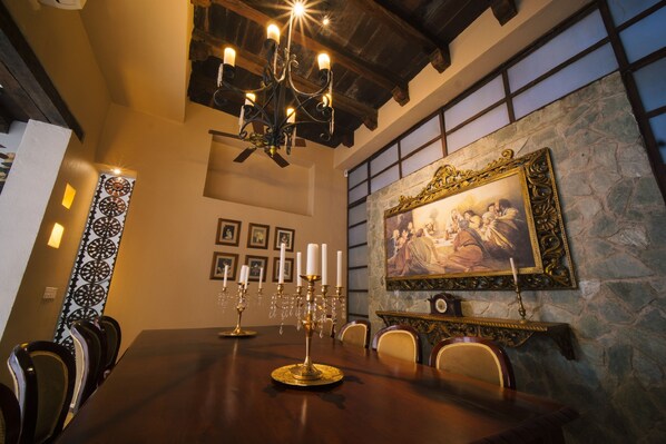 A dining room with a large wooden table, ornate candelabras, and a stone wall with a framed painting.