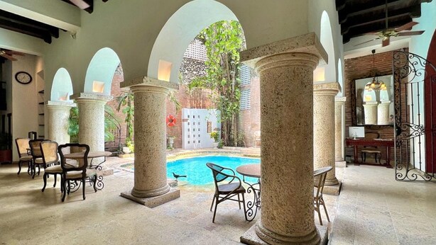 A pool area with stone columns, outdoor seating, and a view of a garden. - 8aps-4 Luxury House in the Historic Center With Pool Air Conditioning and Wifi (Cartagena)