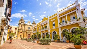 A courtyard with yellow buildings, a clock tower, and potted plants. - 8aps-4 Luxury House in the Historic Center With Pool Air Conditioning and Wifi (Cartagena)