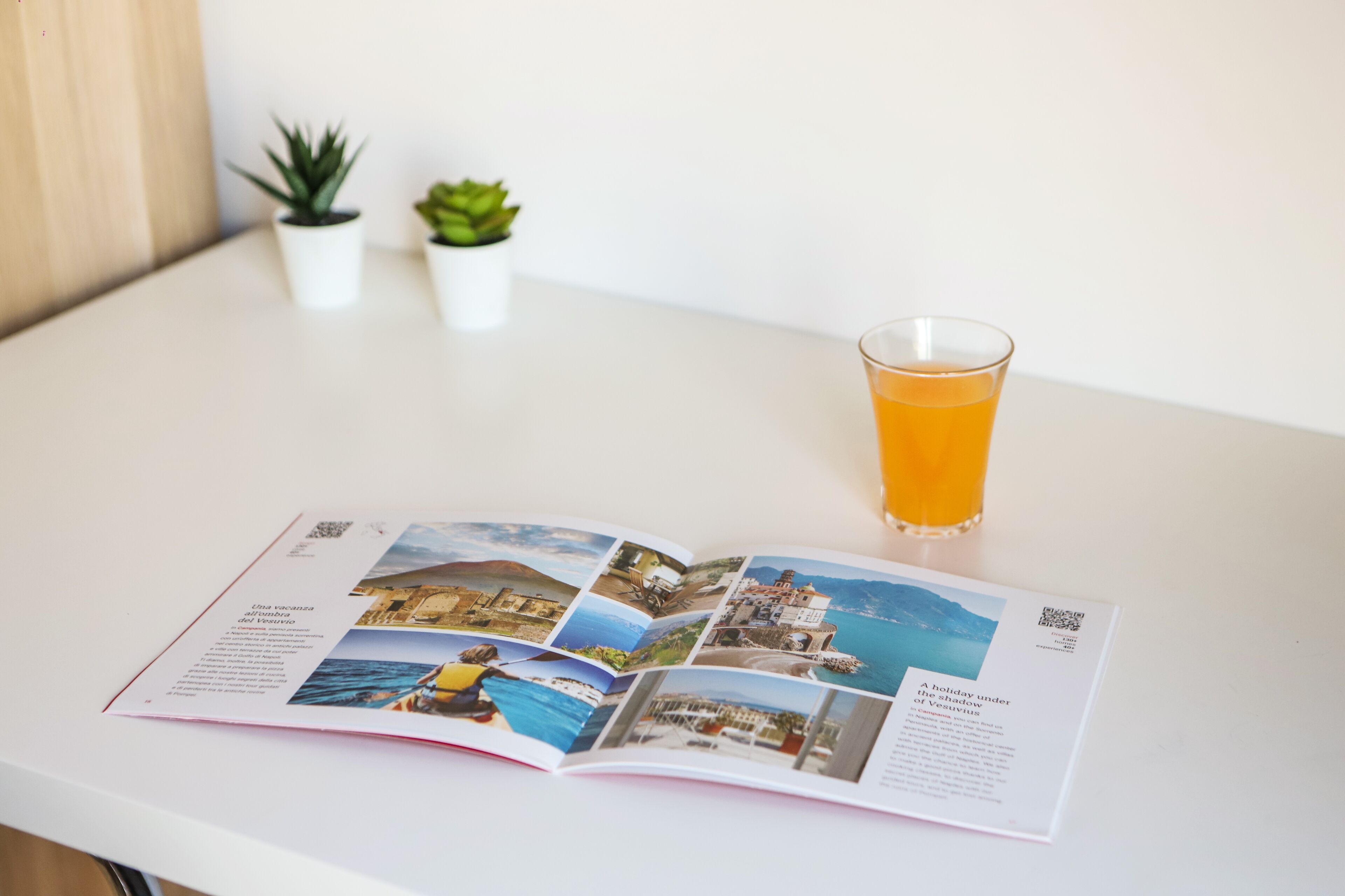 Eine Zeitschrift liegt auf einem Tisch zusammen mit einem Glas Orangensaft, mit Reisefotos und Text.