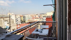 A balcony with a table and chairs, overlooking a cityscape with buildings.