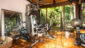 Ett gym med träningsutrustning, en stor spegel och utsikt över grönområden utanför.