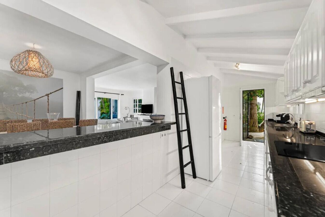 A modern kitchen with white cabinetry, a black countertop, and a hanging light fixture.