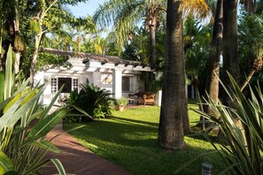 A house with a covered patio, surrounded by palm trees and a well-maintained lawn.