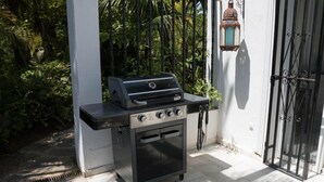 En portabel grill och ugn placerad framför en vit vägg, med ett metallstaket och en lykta.
