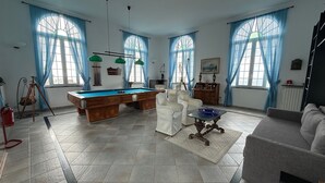 A spacious living room with a pool table, white armchairs, and a grey sofa.