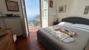 A bedroom with a bed, a nightstand, a dresser, and a view of the sea.