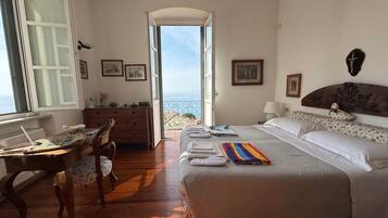 A bedroom with a bed, a desk, a dresser, and a view of the sea.