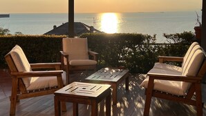 A covered outdoor seating area with a view of the sea at sunset.