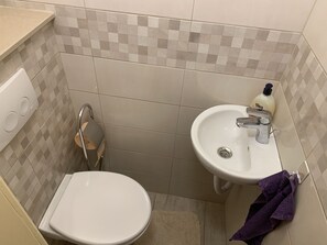 A bathroom with a white toilet, a sink with a soap dispenser, and a towel rack with a purple towel. - Cozy Apartment in the City Center (Zagreb)