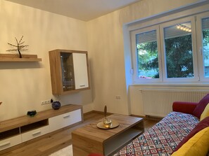Uma sala de estar moderna com um armário de madeira, um aparador com portas de vidro, um sofá estampado e uma janela com vista para árvores.