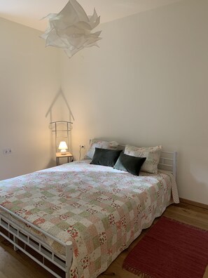 Quarto com cama, almofadas, mesa de cabeceira, abajur e tapete vermelho.