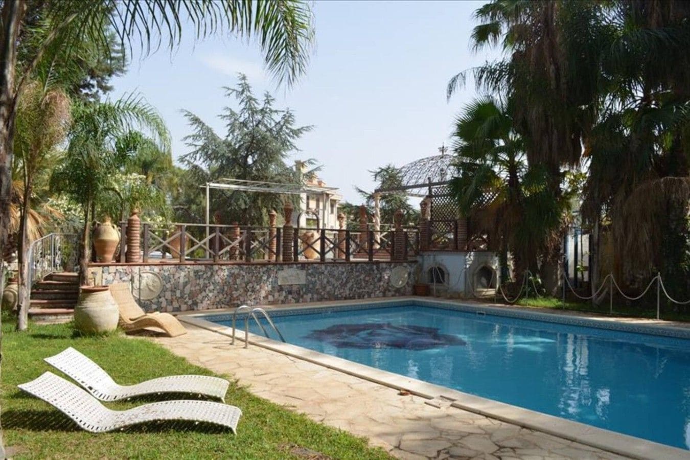 A swimming pool with a stone deck, lounge chairs, and a pergola structure.