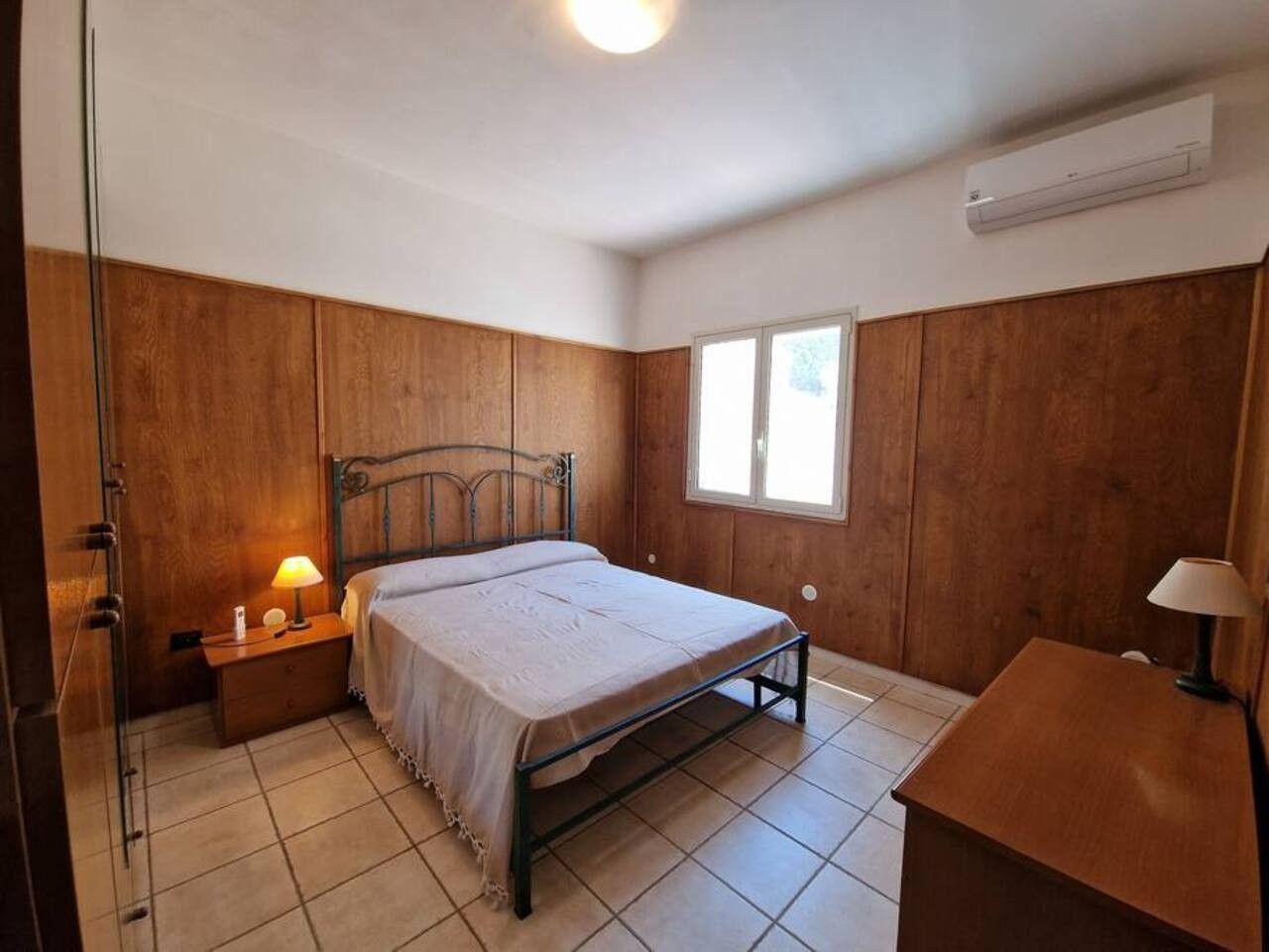 A bedroom with a bed, bedside tables, a window, and wooden paneling.
