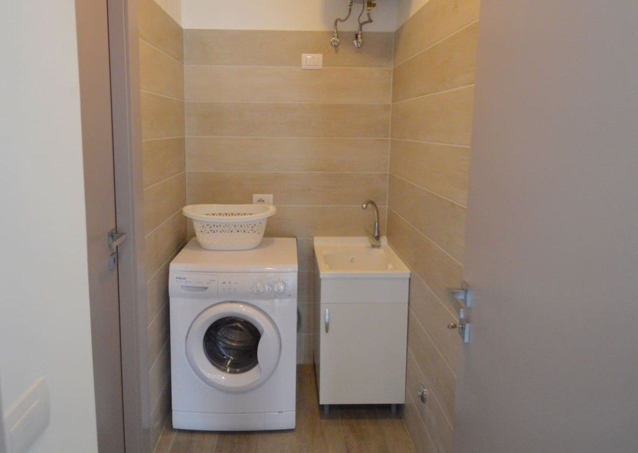 A compact laundry area with a washing machine, a small sink, and a cabinet.