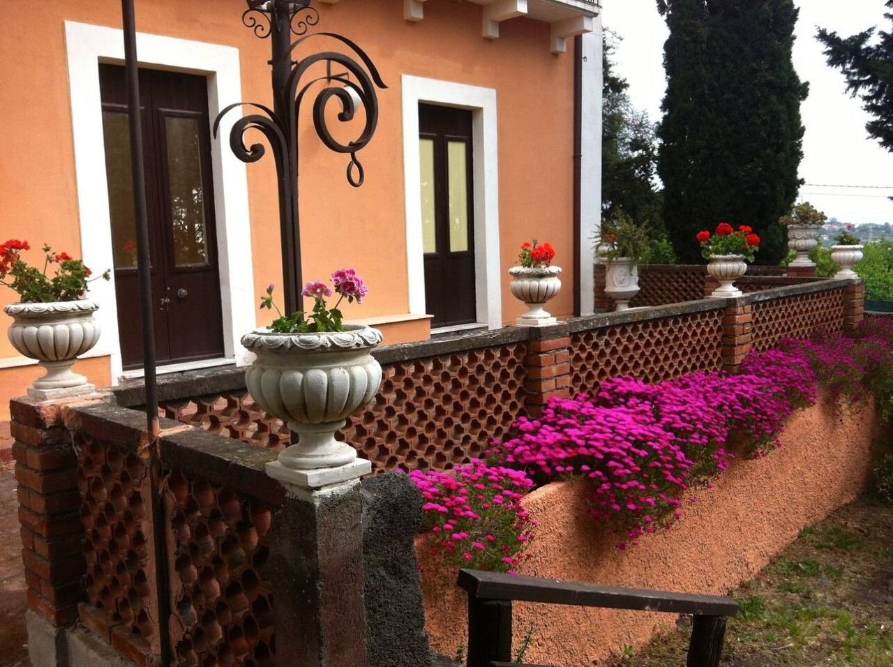 Un edifici amb mur de maó, tanca metàl·lica i testos amb flors roses.