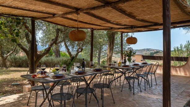 Un espace extérieur aménagé pour les repas, avec des tables et des chaises, une pergola au-dessus et une vue sur la campagne.