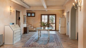 Une pièce spacieuse avec un plafond en bois, une table en verre agrémentée d’une plante en guise de décoration centrale, un tapis à motifs et un meuble avec des tiroirs.