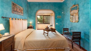Une chambre à coucher avec un lit, une table de chevet avec une lampe, une chaise, une petite table sur laquelle se trouve un plateau avec des éléments pour le petit-déjeuner, et un miroir au mur.