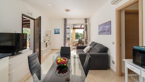A modern living room with a sofa, a TV, and a dining area with a glass table. - VIlla Di Vina - SARDINIA UNLIMITED (Alghero)