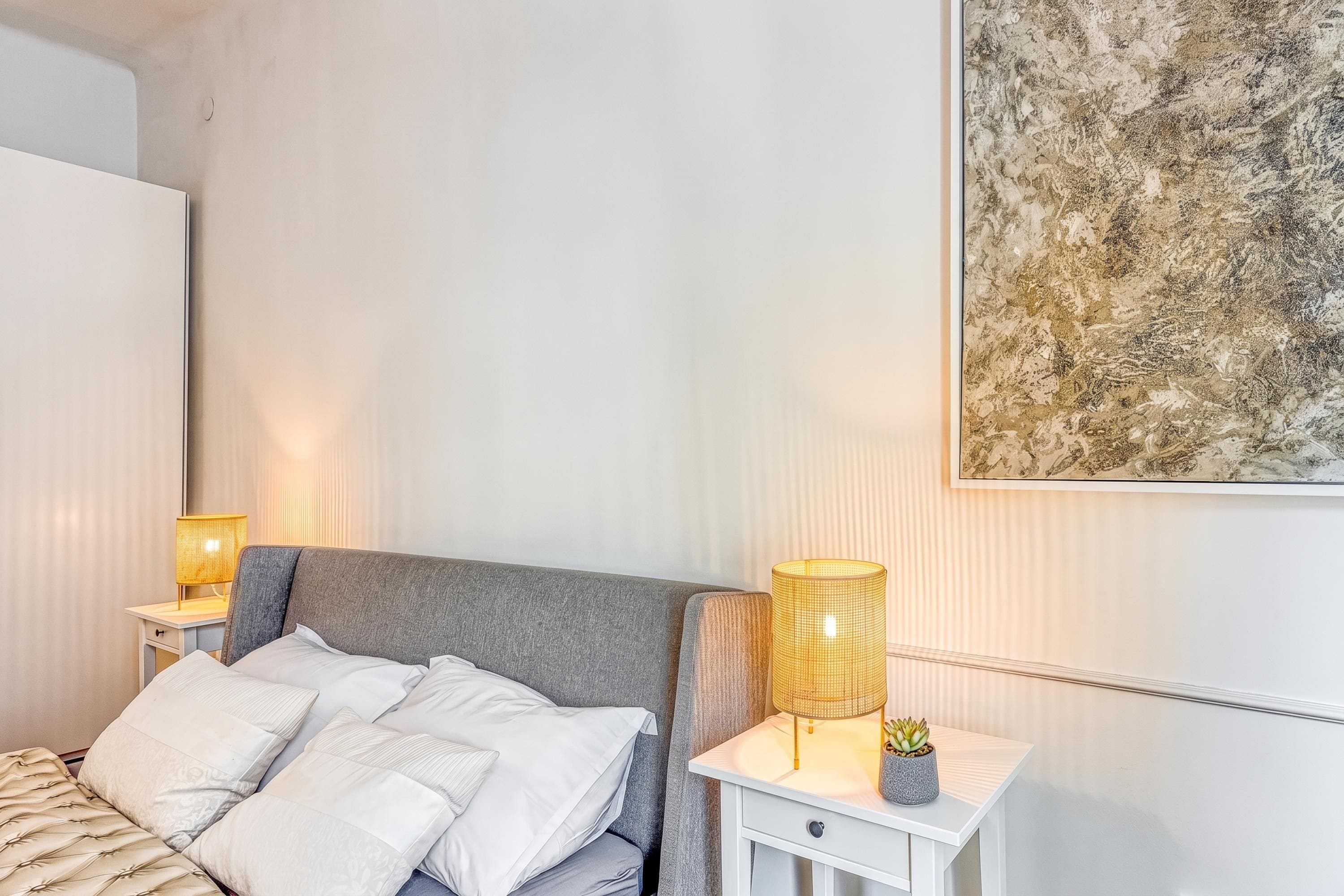 Une chambre d’hôtel avec un lit, des lampes de chevet, une petite table avec une plante et un grand tableau abstrait accroché au mur.