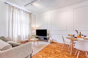 A modern living room with a sofa, a TV, a dining table set for two, and a herringbone wood floor. - Spacious Apartment In Heart Of Zagreb (Zagreb)