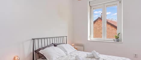 A bedroom with a bed, a bedside table, a lamp, a window with a view, and a hanging light fixture.