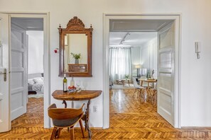 A room with a wooden floor, a dining table with chairs, a mirror, and a bed with pillows.