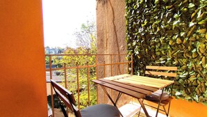 A balcony with a wooden table and chairs, a cushioned bench, and a wall covered in green foliage. - Spacious Apartment In Heart Of Zagreb (Zagreb)