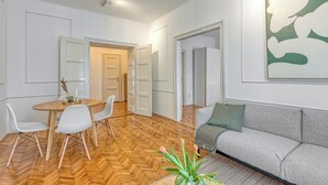 A modern living room with a herringbone floor, a grey sofa, white chairs, and a dining table with a vase of flowers. - Spacious Apartment In Heart Of Zagreb (Zagreb)